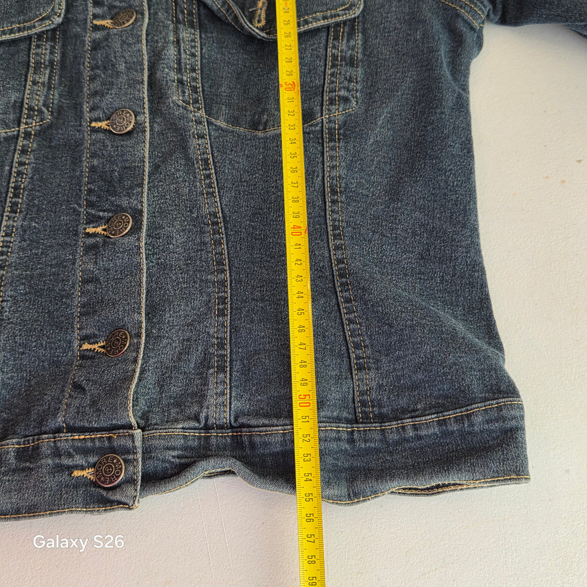 Mesure de la longueur de la veste en jean femme More & More taille 40 avec un mètre ruban jaune.