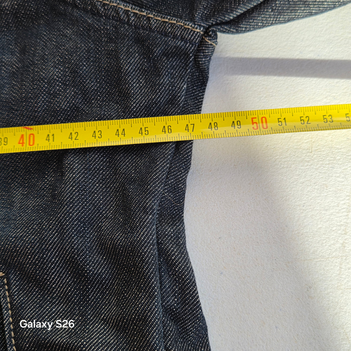 Mesure de la largeur de la veste en jean Jean's U taille 38, présentée avec un mètre ruban.
